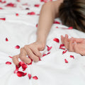 Mulher deitada na cama com pétalas de rosas à sua volta, representando uma relação sexual e o relaxamento após orgasmo