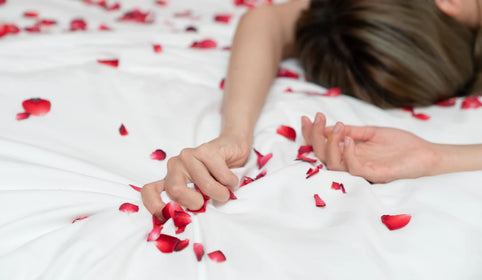 Mulher deitada na cama com pétalas de rosas à sua volta, representando uma relação sexual e o relaxamento após orgasmo
