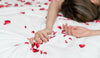 Mulher deitada na cama com pétalas de rosas à sua volta, representando uma relação sexual e o relaxamento após orgasmo